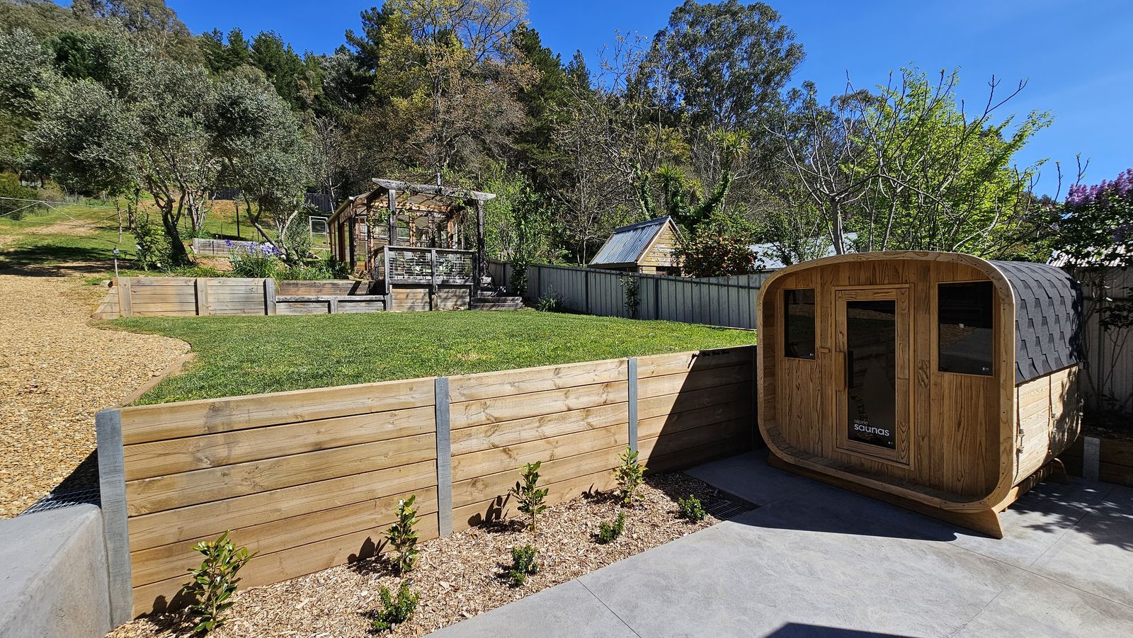 The fully fenced yard: lawn, timber retaining walls and the sauna, with the bush rising behind the back fence