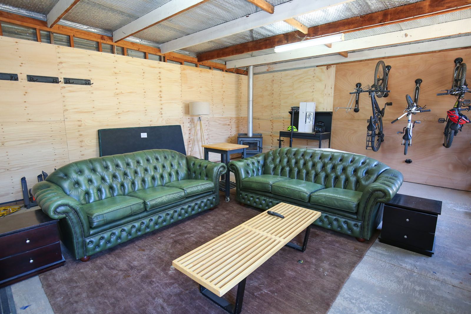 The garage lounge: two green leather sofas, a low table, the second wood heater, and bike racks on the wall behind