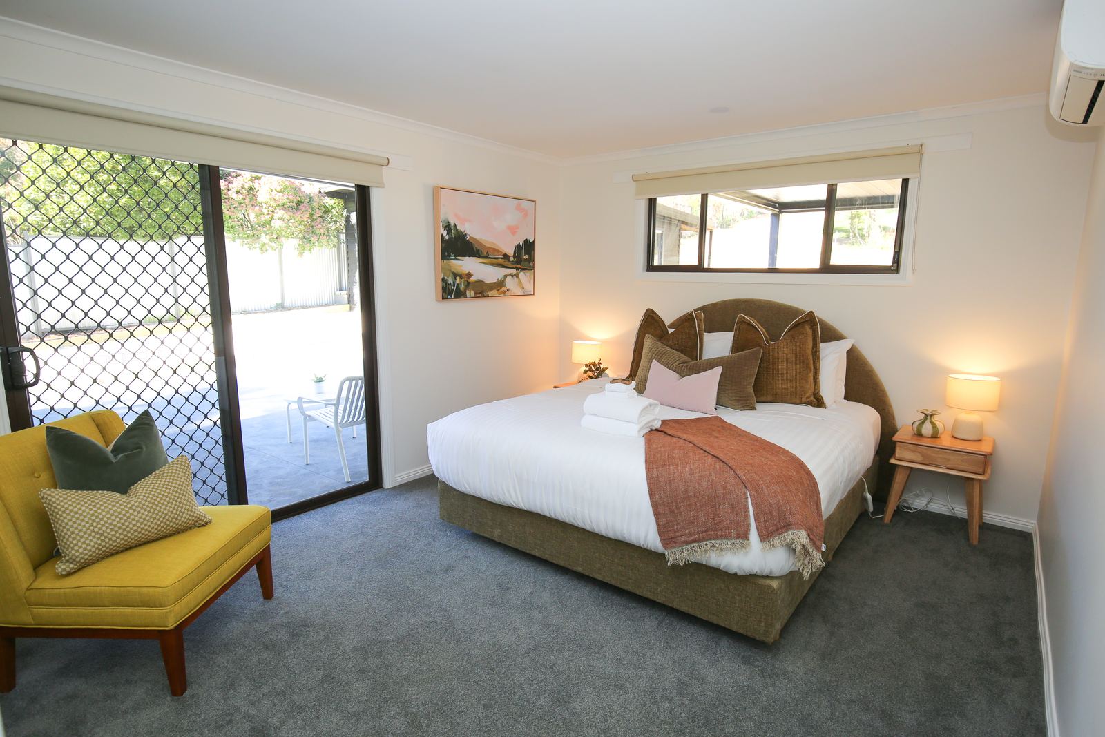 The main bedroom: a king bed with a mustard armchair and sliding doors out to the yard